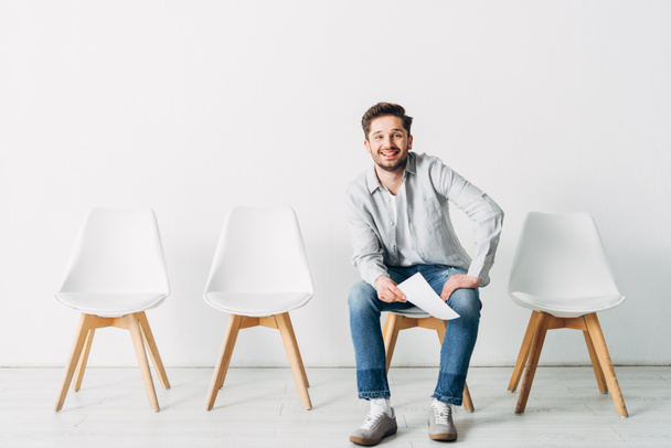 Smiling man with resume looking at camera while sitting on chair in office - Photo, Image