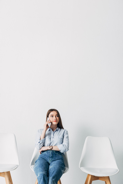 Hermosa mujer joven hablando en el teléfono inteligente mientras espera entrevista de trabajo en la oficina
  - Foto, Imagen