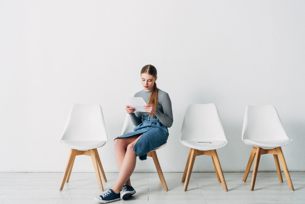 Aantrekkelijke werknemer lezen CV in de buurt van smartphone op stoel in het kantoor  - Foto, afbeelding
