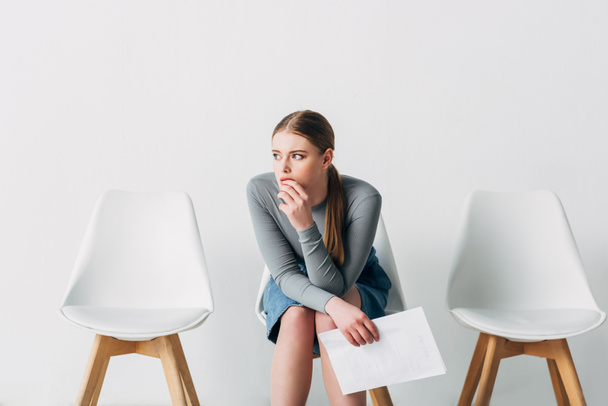 オフィスで椅子に座っている間に履歴書を持っている思考の女性  - 写真・画像