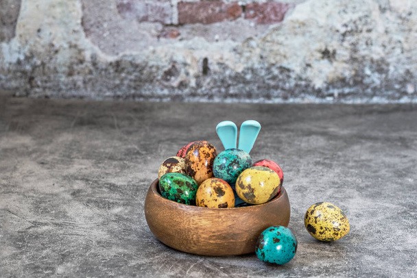 Szczęśliwej Wielkanocy, przepiórki malowane cętkowane jaja w drewnianej misce na niebieskim betonowym tle i uszy królika, symbol wiosennego święta prawosławnego i katolickiego. - Zdjęcie, obraz