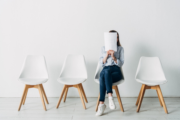 Young woman covering face with resume while waiting for job interview in office  - Foto, imagen