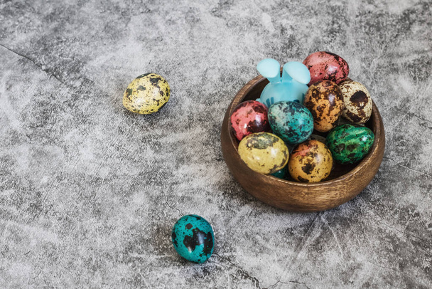 Happy Easter, quail painted spotted eggs in a wooden bowl on a blue concrete background and rabbit ears, a symbol of the spring Orthodox and Catholic holiday. - Photo, image