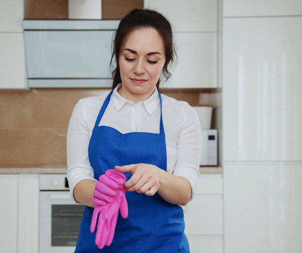 Young beautiful girl puts on pink gloves for cleaning. The girl is engaged in cleaning. Professional cleaning - Foto, afbeelding
