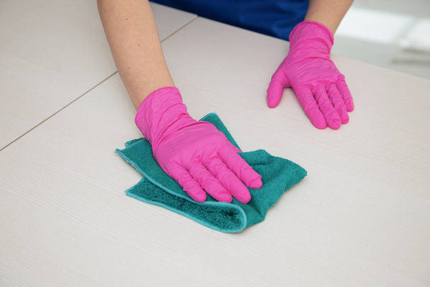 Uma mão em uma luva rosa limpa uma superfície branca com um trapo azul para limpar
. - Foto, Imagem