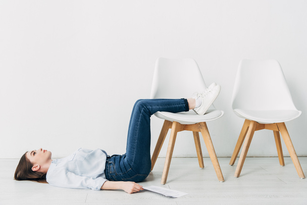 Vista lateral do empregado deitado no chão perto de currículo e cadeira no escritório
  - Foto, Imagem