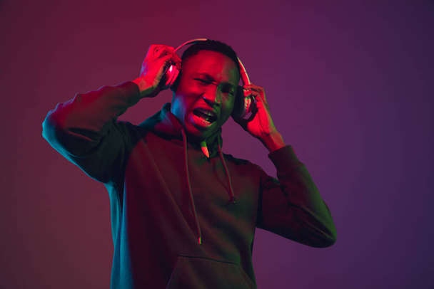 African-american mans portrait with headphones isolated on gradient studio background in neon light - 写真・画像