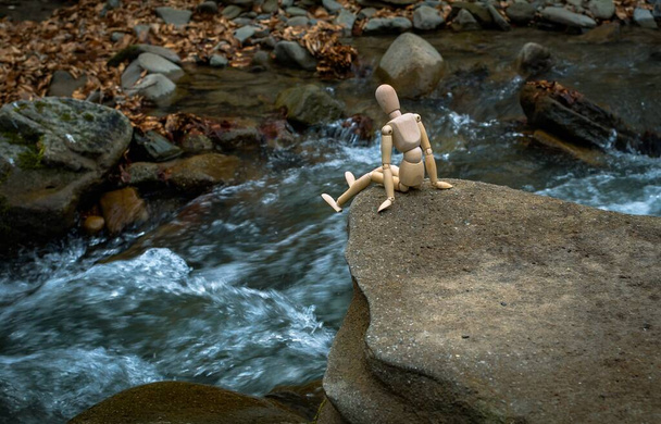 Homem pequeno articulado senta-se em uma pedra acima de um rio de montanha
 - Foto, Imagem