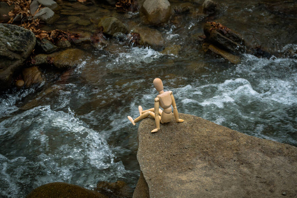 Articulated little man sits on a stone above a mountain river - Photo, Image