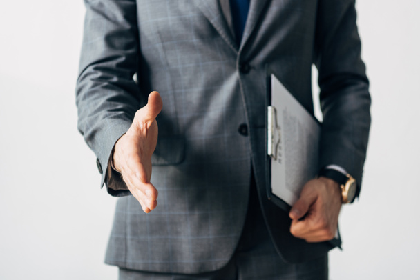 Cropped view of employee in suit holding clipboard and pulling hand for handshake isolated on grey - Fotografie, Obrázek