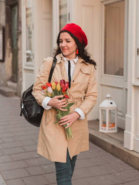 Красивая молодая женщина с весенним букетом цветов тюльпанов на городской улице. Счастливая девушка гуляет на улице. Весенний портрет красивой женщины в парке
. - Фото, изображение