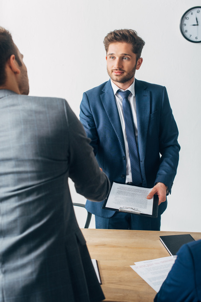 Selective focus of recruiter with clipboard shaking hands with employee in office  - Photo, Image