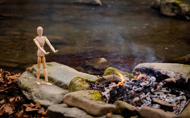 Un ometto articolato si scalda davanti al fuoco sulle rive di un fiume di montagna
 - Foto, immagini