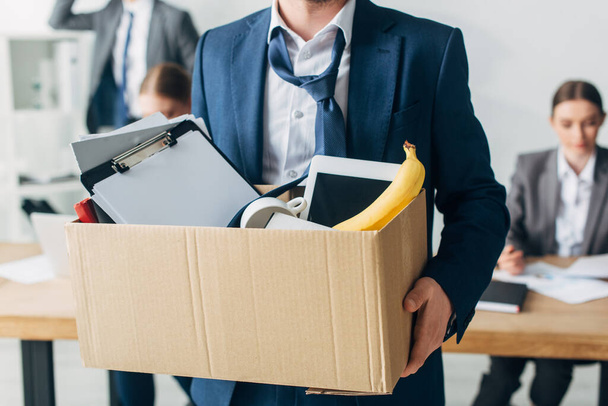 Selektywne skupienie się na odrzuconym człowieku trzymającym kartonowe pudełko z papierami, tabletem cyfrowym i bananem w biurze  - Zdjęcie, obraz