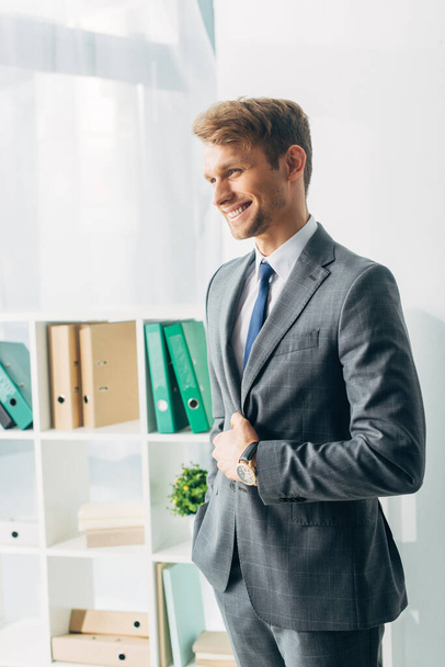 Hezký obchodník v obleku se usmívá v kanceláři  - Fotografie, Obrázek