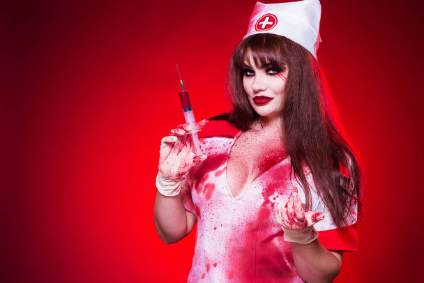 Beautiful, sexy, a woman in a nurse's suit, with a large notch on the chest holding a syringe with blood. The girl in the medical gown is covered in blood. Nurse Killer. ?ostume party Halloween - Photo, Image