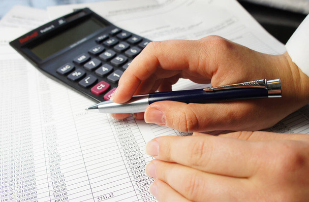 Калькулятор, ручка и бухгалтерский документ с большим количеством цифр и женские руки
 - Фото, изображение