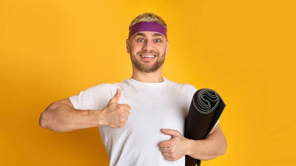 Lächelnder Mann mit Sportmatte zeigt Daumen hoch - Foto, Bild