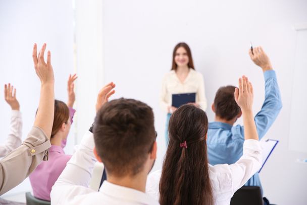 Ihmiset nostavat kätensä esittämään kysymyksiä sisätiloissa järjestettävässä yrityskoulutuksessa
 - Valokuva, kuva