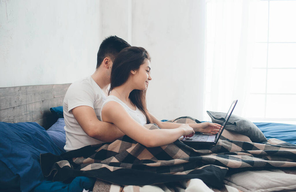 Mladí muži a ženy pracují na počítači nebo hledají informace na internetu na posteli. - Fotografie, Obrázek