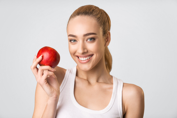 Fille avec dents blanches tenant la pomme rouge sourire, fond gris
 - Photo, image