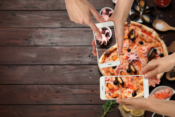 Food bloggers taking pictures of delicious seafood pizza at wooden table, closeup. Space for text - Photo, Image