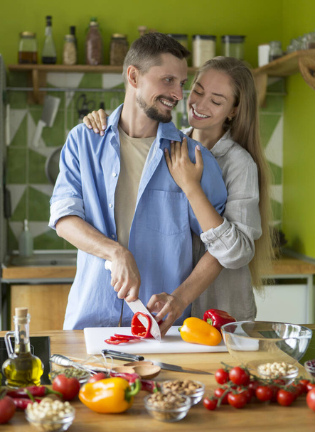 Embracing couple making delicious fresh salad of vegetables - 写真・画像