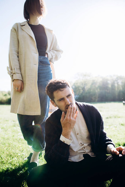 Hombre joven fumando cigarrillo en el campo verde, mujer en el fondo
 - Foto, imagen