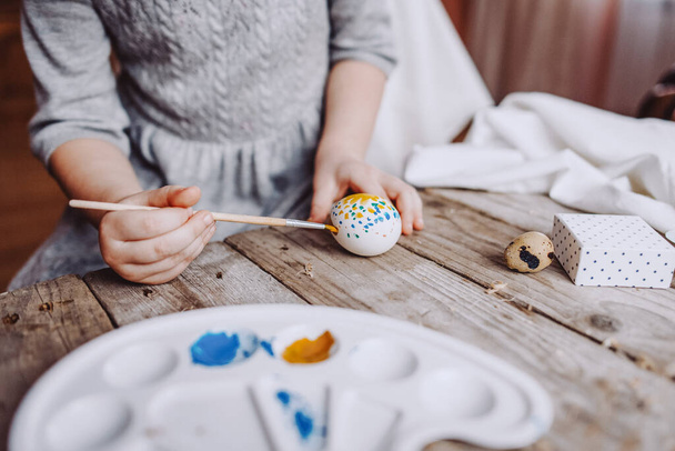 Frohe Ostern! Nettes kleines Mädchen bemalt Eier mit blauer und gelber Farbe mit Chaos auf dem Tisch - Foto, Bild
