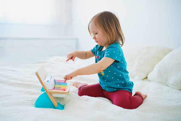 Adorable little girl playing toy piano at home, in kindergaten or preschool. Creative games, education and distance learning for kids. Stay at home entertainment - Photo, image