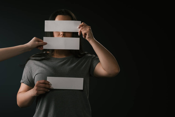 Front view of plus size girl covering face under empty cards with copy space on black background - Photo, Image