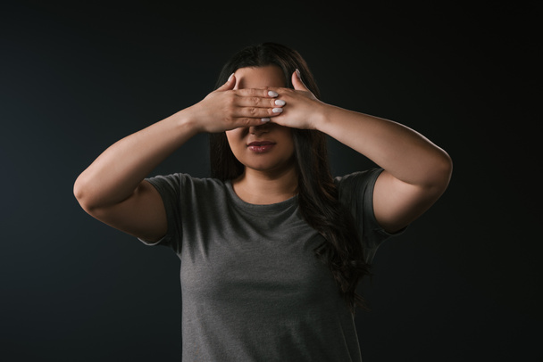 Front view of plus size girl covering eyes with hands on black background  - Fotografie, Obrázek