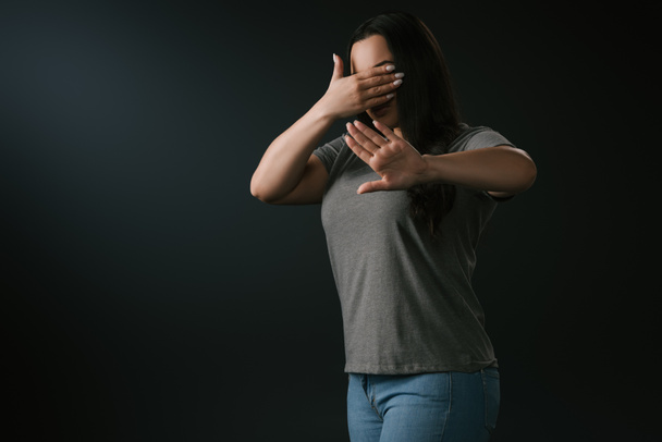 Plus size girl expressing blindness and denial with stop gesture isolated on black - Fotó, kép