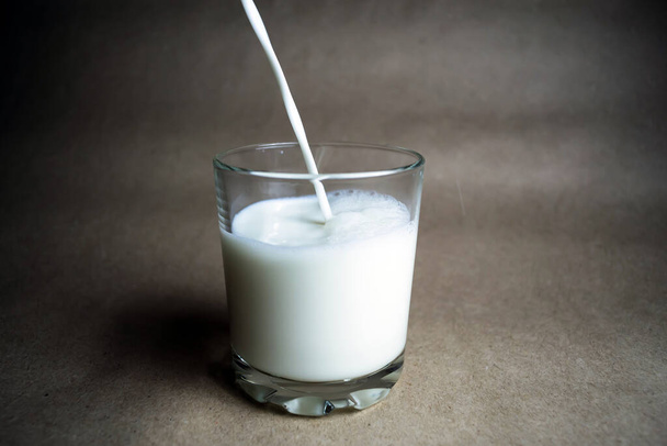 Het proces van het gieten van melk in een glas. Beige achtergrond - Foto, afbeelding