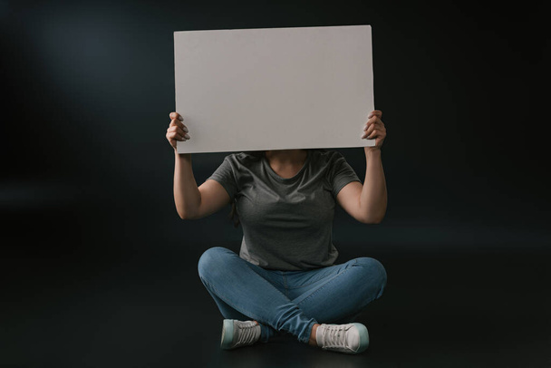 Front view of plus size girl sitting with empty board on black background - Photo, Image