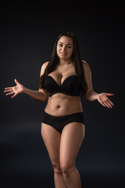 Smiling plus size girl in underwear with outstretched hands on black background - Fotografie, Obrázek