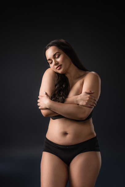 Front view of plus size girl enjoying and hugging her body on black background - Photo, Image