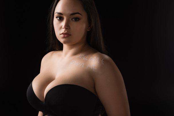 Portrait of plus size model in bra with lettering You Don't Own Me on body isolated on black - Foto, afbeelding