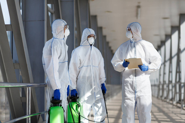 Homens em trajes de proteção contra vírus planejando desinfetar a cidade
 - Foto, Imagem