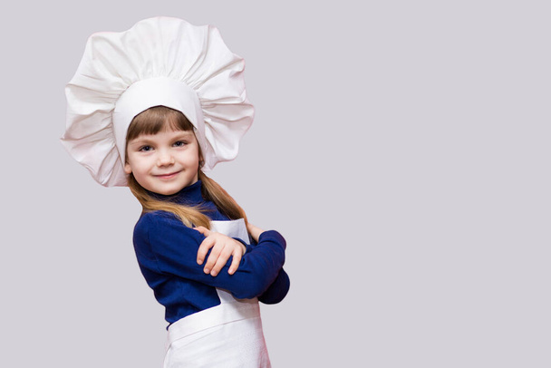 Портрет улыбающейся девушки-повара в форме с крестиком на белом фоне. Детский повар. Концепция процесса приготовления пищи
 - Фото, изображение