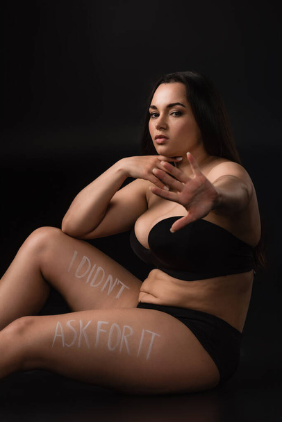 Plus size model in underwear with stop gesture and lettering I Did not Ask For It on body on black background - Photo, Image