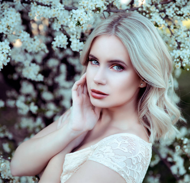 Portrait of young woman posing on blooming tree background - Valokuva, kuva