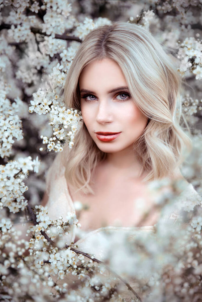 Portrait of young woman posing on blooming tree background - Photo, Image