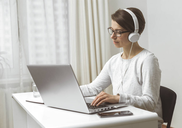 Kobieta-wolny strzelec pracuje w odległym domu. Kobieta studiuje wideo czat na laptopie. Dziewczyna w słuchawkach komunikuje się przez połączenie wideo. - Zdjęcie, obraz