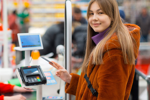 Young woman with a credit card pays for purchases at the checkout counter in the store - Photo, Image
