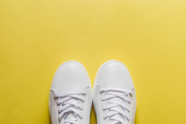 Пара белых кожаных кроссовок на жёлтом фоне. Копирование пространства
. - Фото, изображение