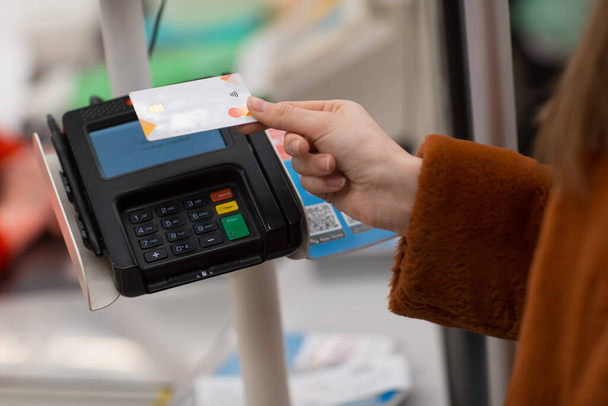 Молодая женщина с кредитной картой оплачивает покупки в кассе в магазине
 - Фото, изображение