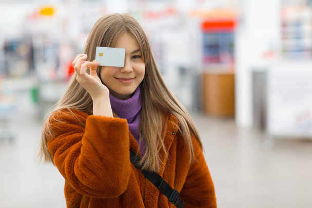 Молода жінка тримає кредитну картку в руках біля обличчя
 - Фото, зображення