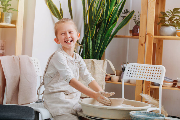 Portrait of a boy, he makes a bowl behind a potter's wheel, laughing looks into the camera - Photo, image