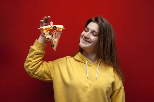 giovane allegra ragazza divertente tiene un pezzo di deliziosa pizza e sorrisi su uno sfondo colorato, adolescente felice con fast food, primo piano
 - Foto, immagini